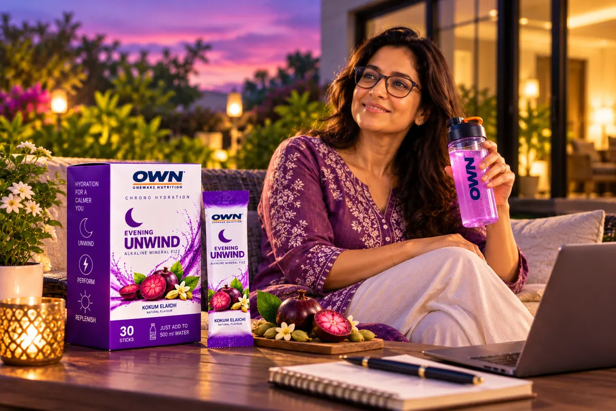 A woman relaxing on a terrace at dusk with an OWN Chrono bottle beside the Evening Unwind carton and stick, with kokum and cardamom